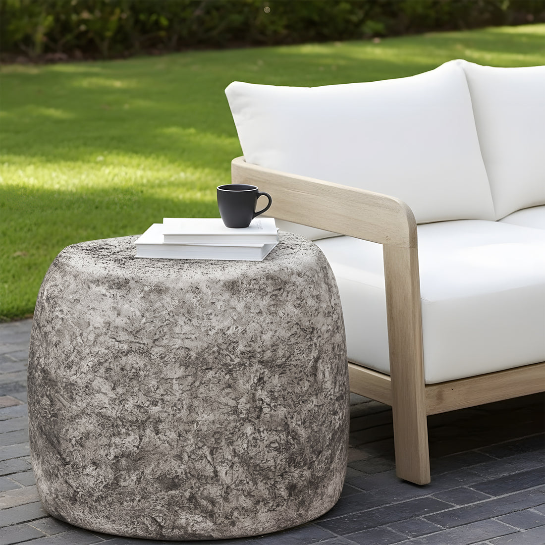 Round outdoor side table with a heavily textured grey stone finish, positioned next to a timber-framed lounge.