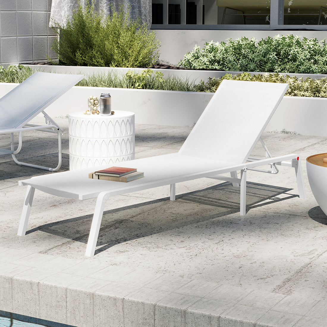 Jabari Textilene Aluminium Outdoor Sunbed in Cream White with adjustable backrest, white metal frame, and two stacked books. Nearby, a side table with tumbler and jar, set by a pool.