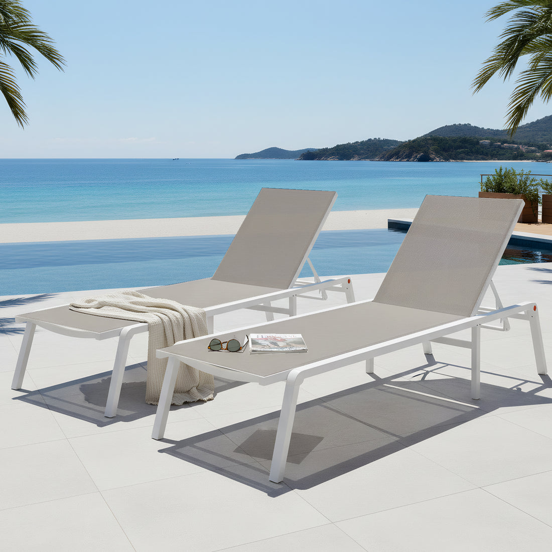 Pair of white aluminum outdoor sun loungers with light grey textilene mesh seating, positioned poolside with an ocean view.