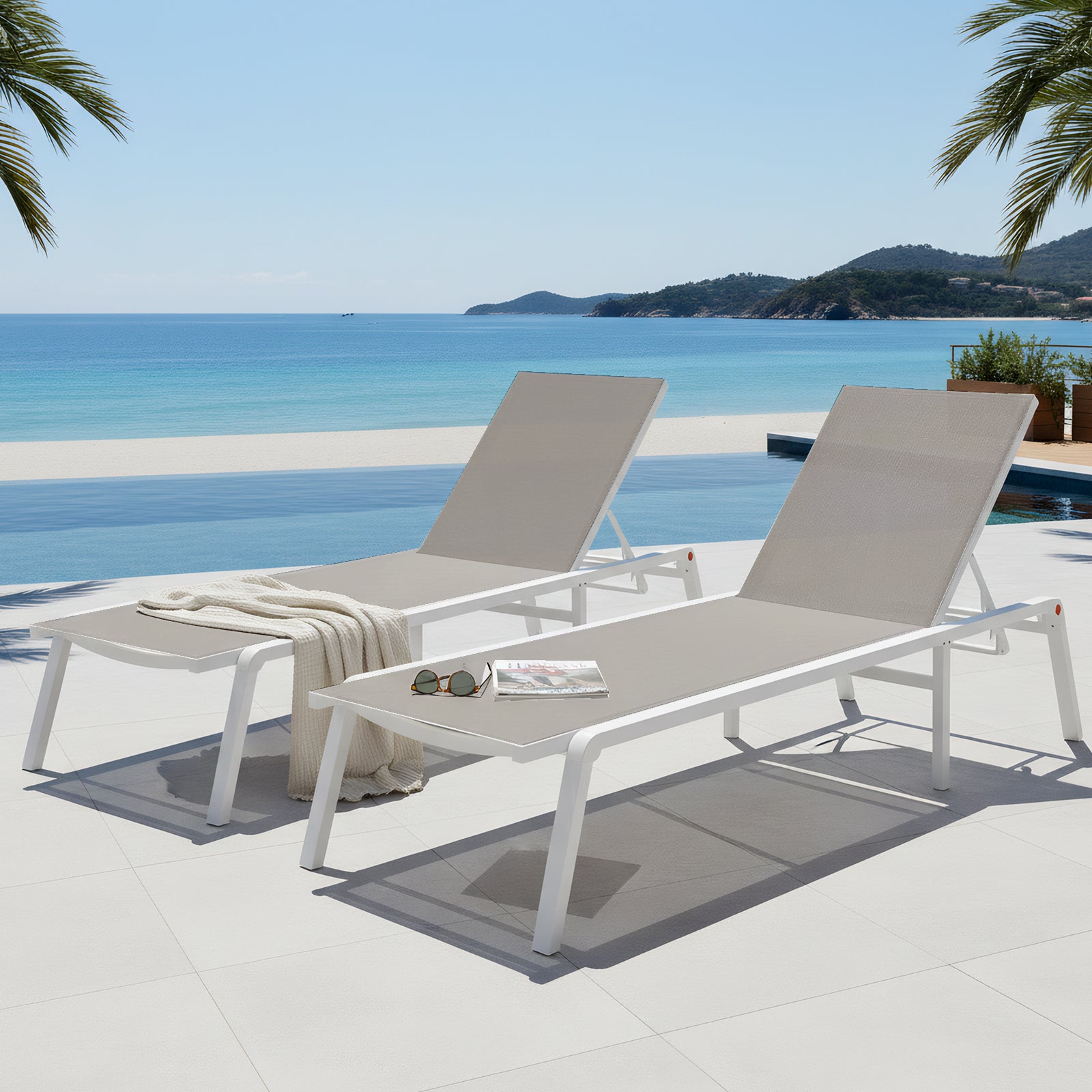 Pair of white aluminum outdoor sun loungers with light grey textilene mesh seating, positioned poolside with an ocean view.