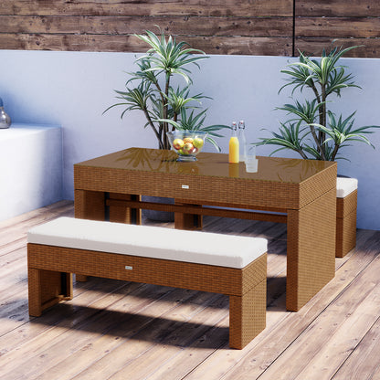 Kummi 4 Seater Outdoor Dining Bench Set features a wicker table with a glass top, two matching benches with cushions, a fruit bowl, and potted plants, creating a stylish outdoor setup.