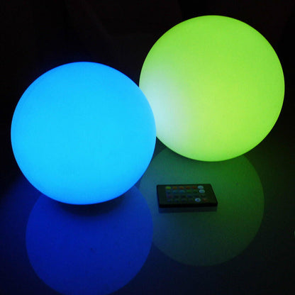 Waterproof Outdoor LED Ball Lights Décor 50cm alongside a remote control on a table, showcasing its sleek, spherical design perfect for enhancing outdoor spaces like pools or gardens with vibrant lighting.