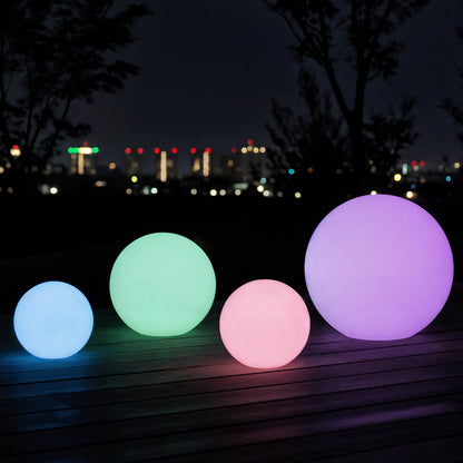 Sphero 60cm Floating Waterproof Outdoor LED Ball Lights on a deck at night, glowing in various sizes. Ideal for gardens or pools, with a distant city skyline in the background.