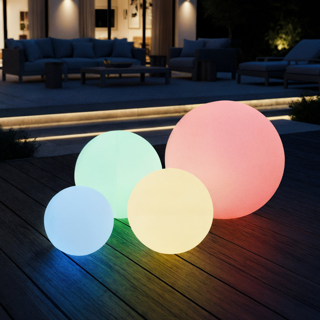 Sphero 60cm Floating Waterproof Outdoor LED Ball Lights glow in blue, green, yellow, and pink on a nighttime patio, resting on a wooden deck, enhancing the outdoor ambiance with their enchanting presence.