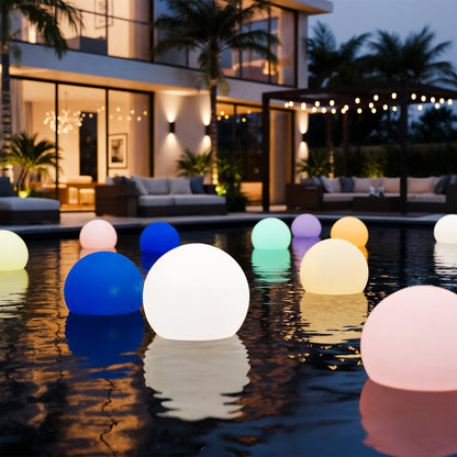 Sphero 60cm Floating Waterproof Outdoor LED Ball Lights illuminating a modern pool area at night, creating an ambient glow. The contemporary setting includes a two-story house and tropical plants.