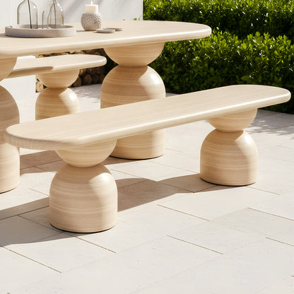 Outdoor bench with a rounded timber-grain top and dual sculptural, hourglass-shaped pedestal bases on a stone patio.