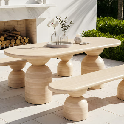 Outdoor bench with a rounded timber-grain top and dual sculptural, hourglass-shaped pedestal bases on a stone patio.