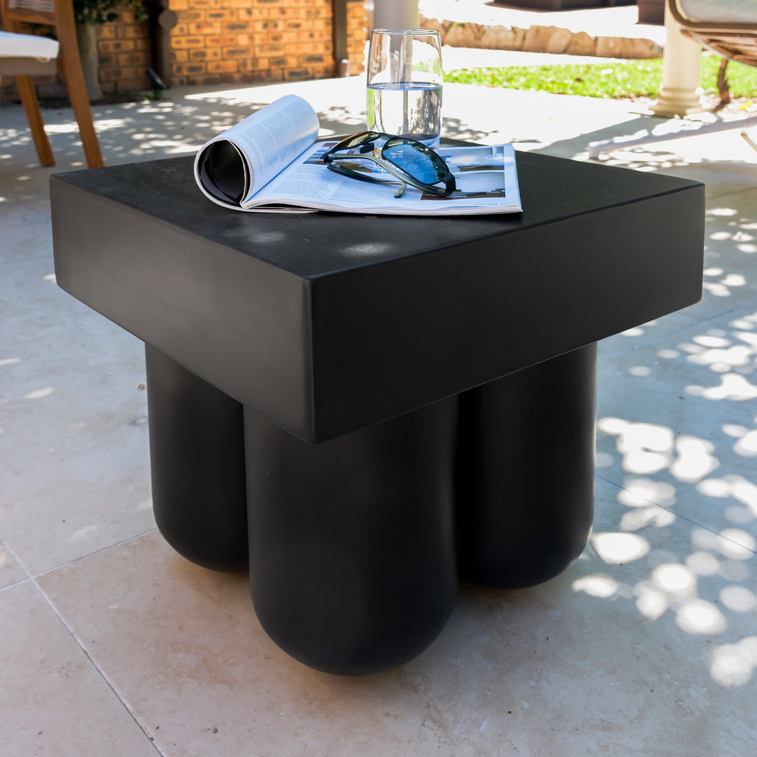 Rissa Indoor & Outdoor Cone Base Concrete Side Table on a coffee table, featuring a square top with four cone legs, alongside a glass of water, magazine, and sunglasses.