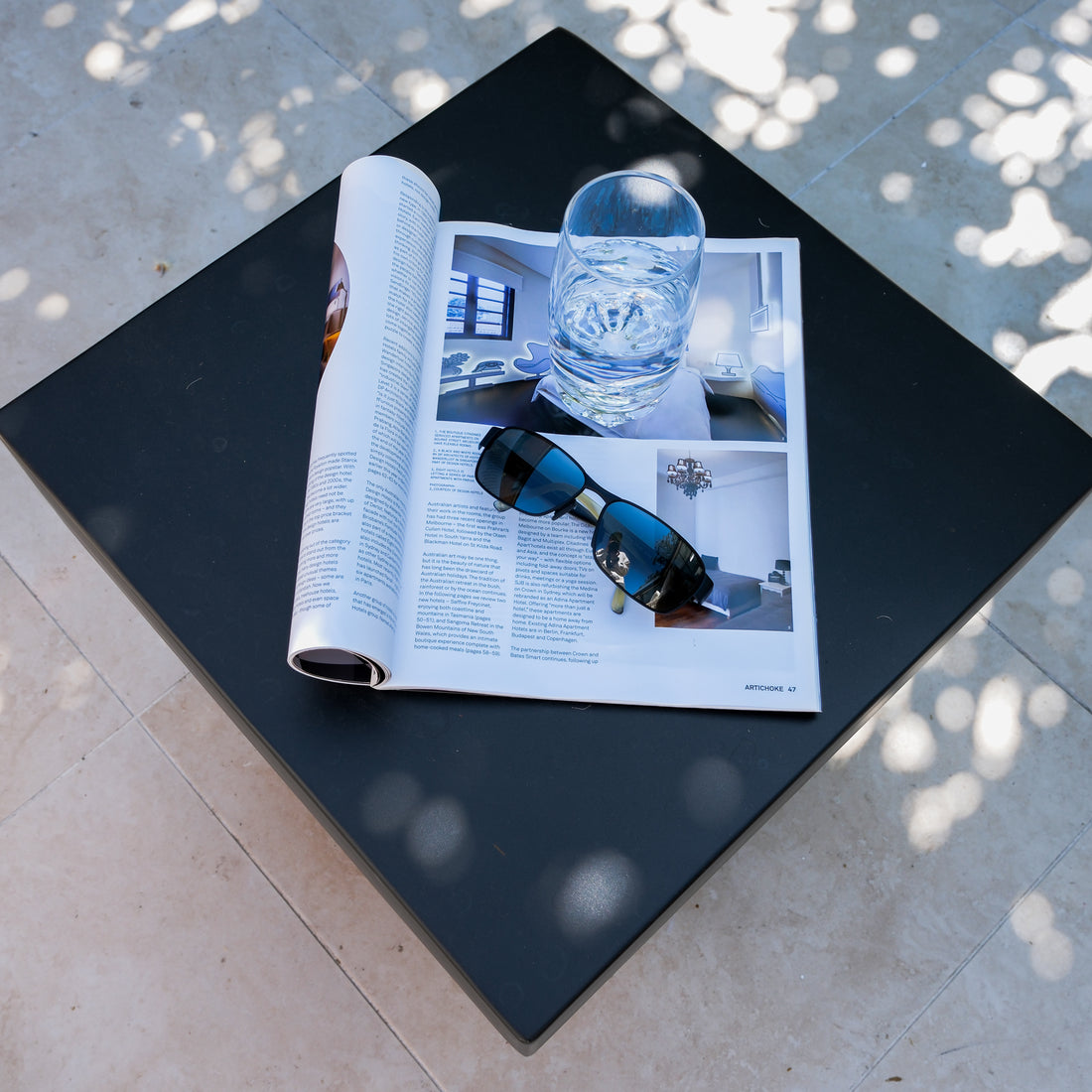 Rissa Indoor & Outdoor Cone Base Concrete Side Table Black featuring a square tabletop with sunglasses and a magazine on it, showcasing its sleek design and practical use for indoor and outdoor settings.