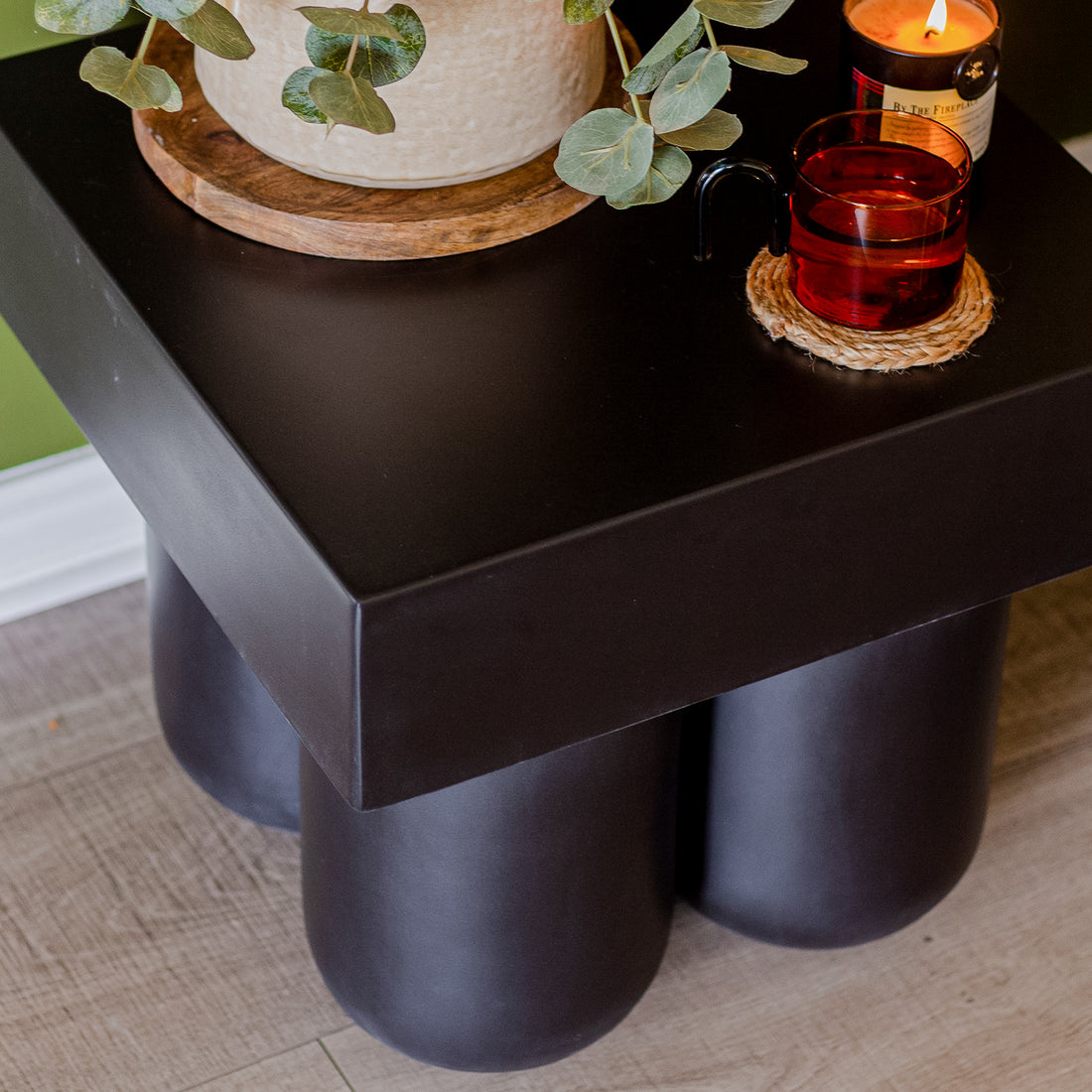Rissa Indoor & Outdoor Cone Base Concrete Side Table Black, featuring a square tabletop on four cone-shaped legs, displayed on a coffee table holding a plant and glass.