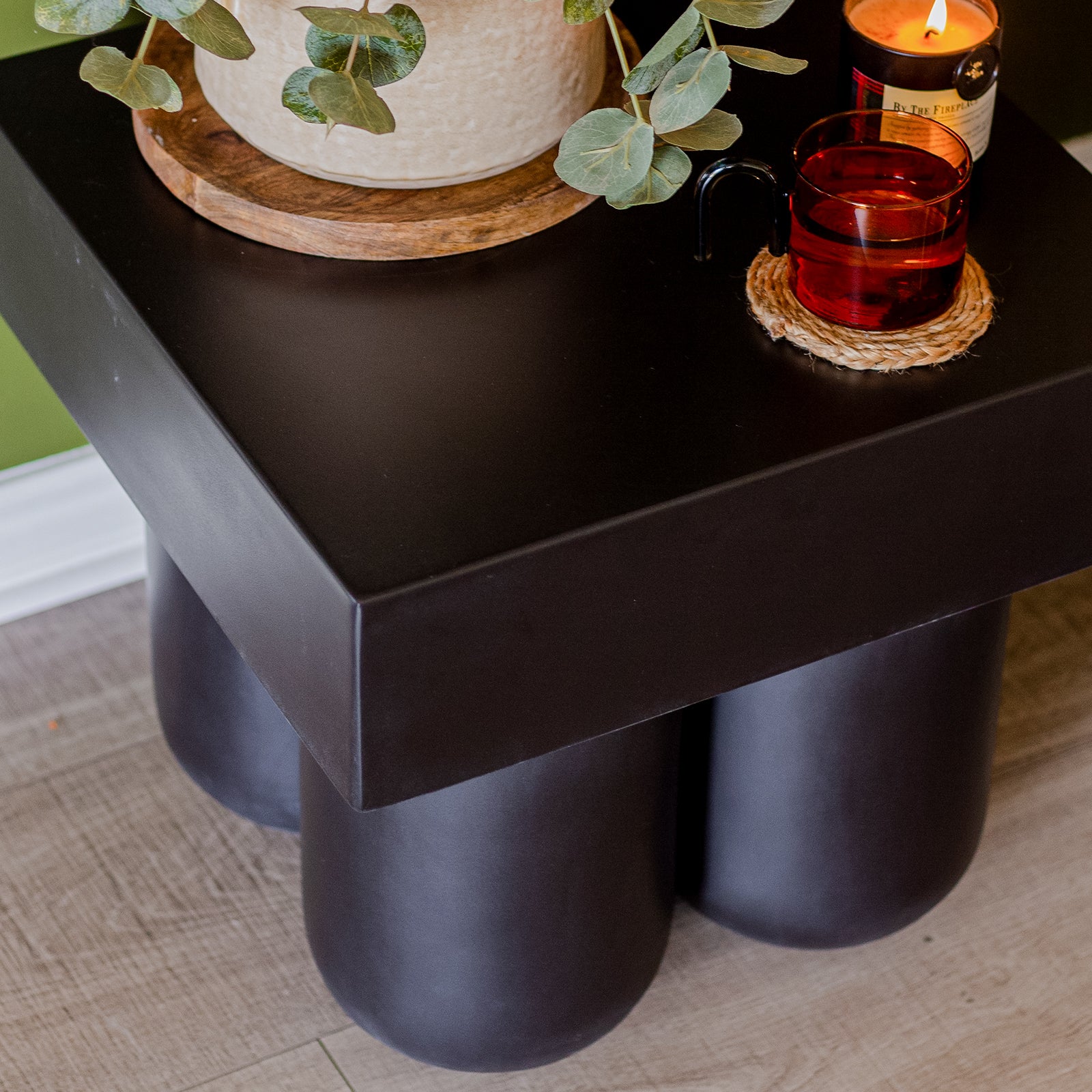 Rissa Indoor & Outdoor Cone Base Concrete Side Table Black, featuring a square tabletop on four cone-shaped legs, displayed on a coffee table holding a plant and glass.
