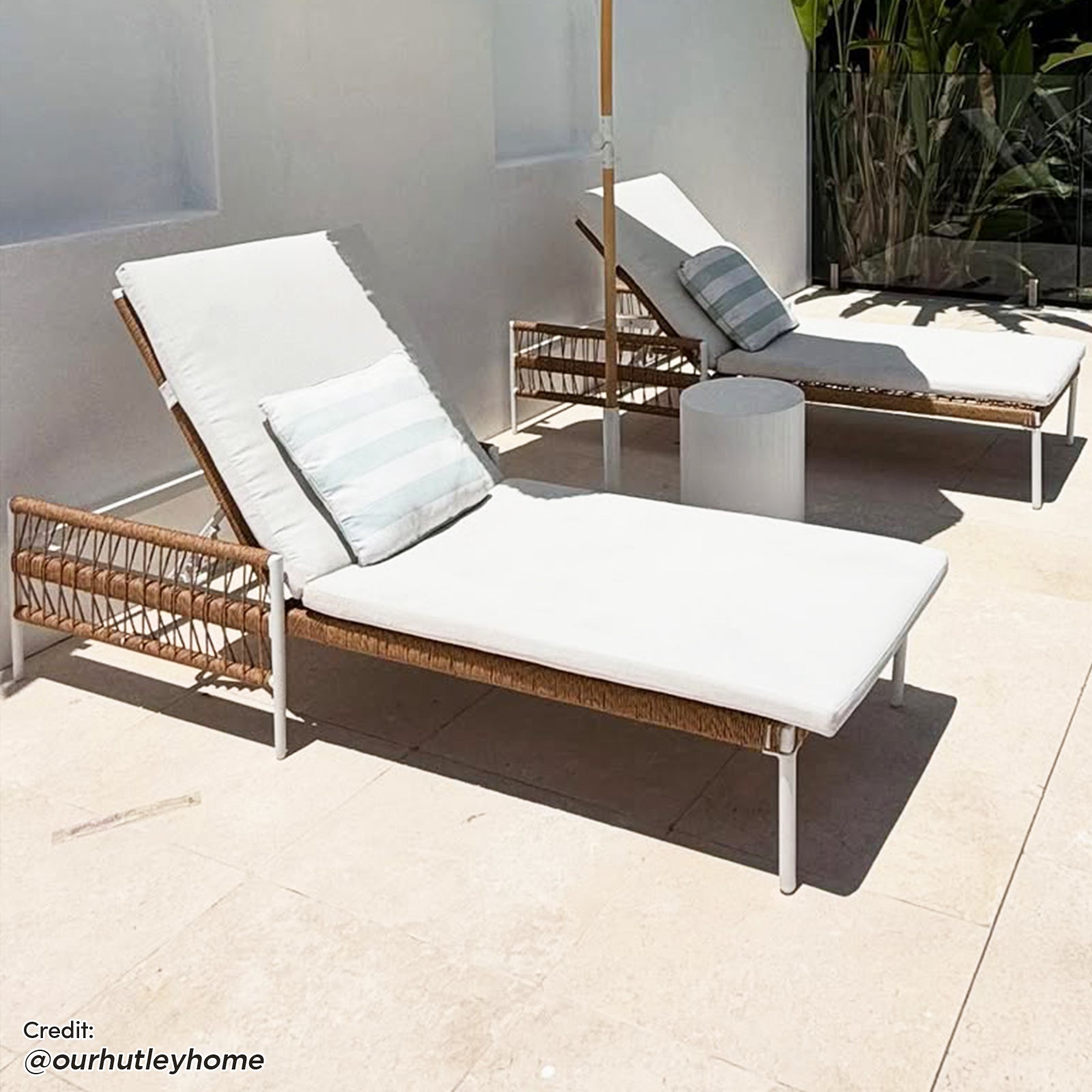 Sibutu Wicker Outdoor Sun Loungers in Light Beige feature woven-rope frames, thick white cushions, striped pillows, and slim metal legs, perfect for elegant patio relaxation with a round side table nearby.
