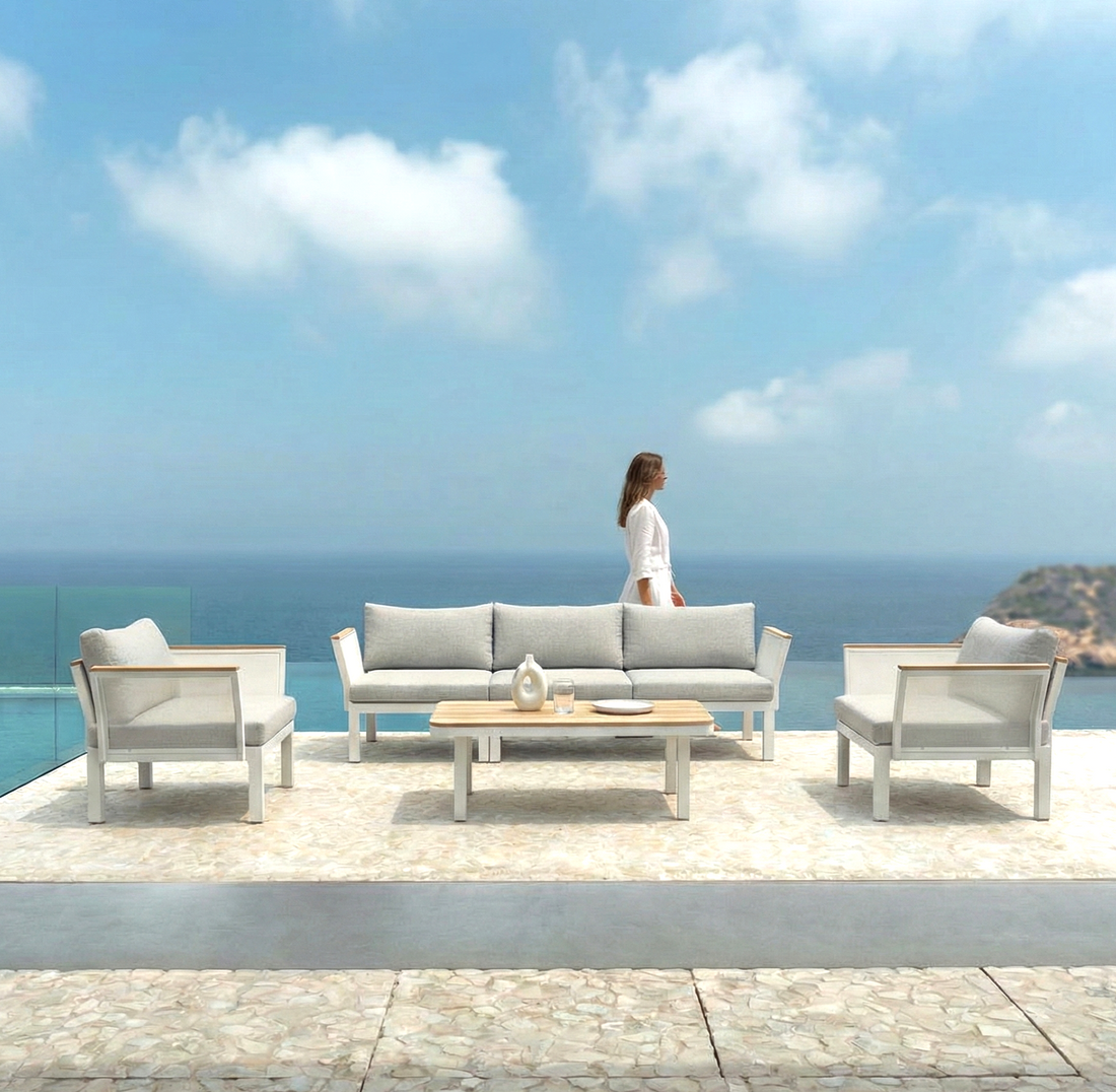 Sierra 5-Seater Outdoor Lounge Set with a sofa, two armchairs, and coffee table on a seaside terrace, overlooking an infinity pool and ocean, with a woman walking nearby.