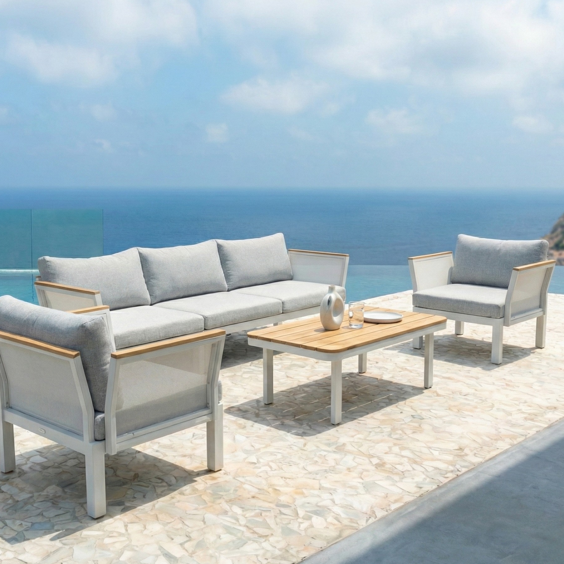 Sierra 5-Seater Outdoor Lounge Set in Grey: Features a three-seat sofa, two armchairs with pale grey cushions, and a slatted wood coffee table, set against a seaside view.