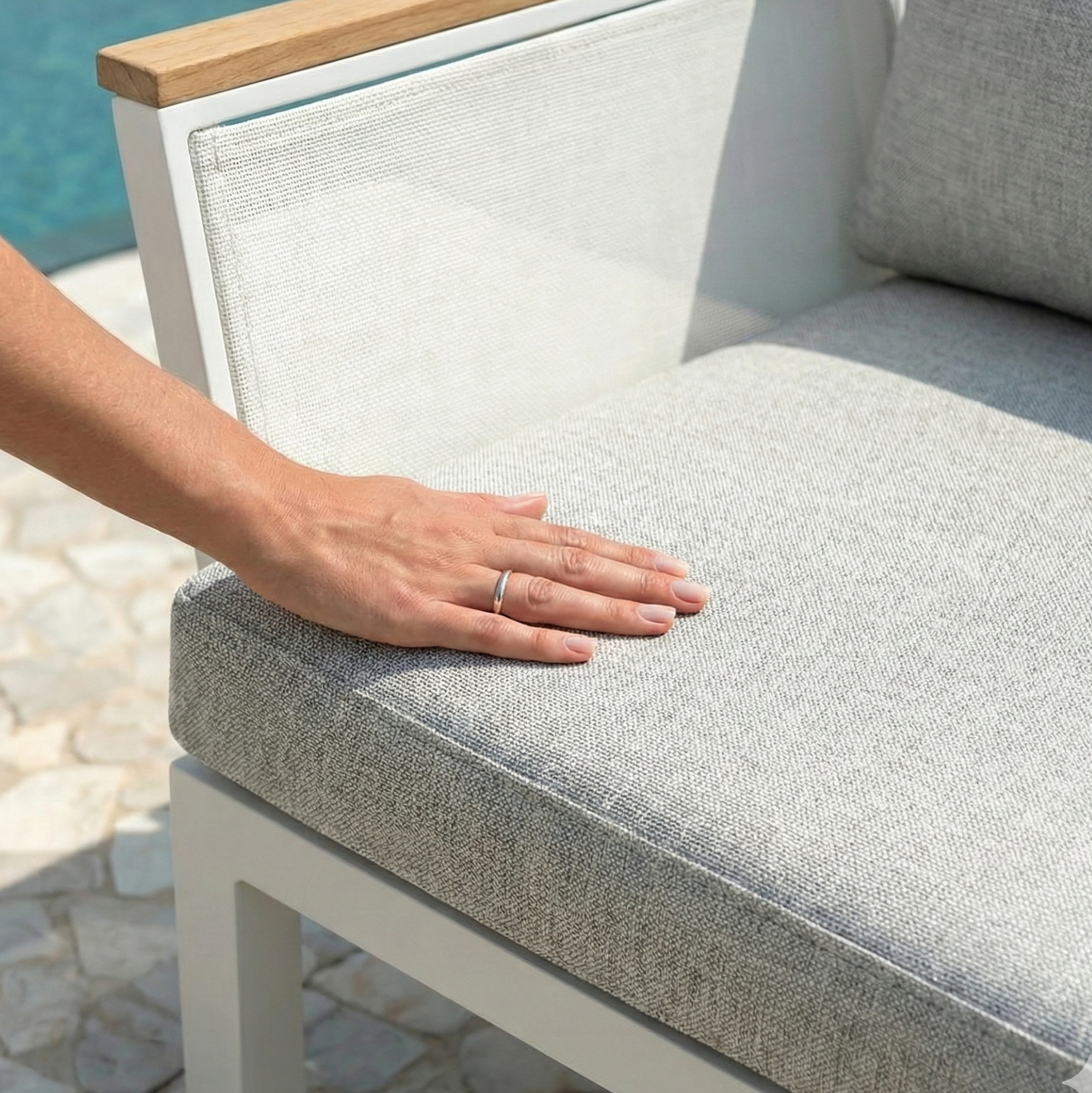 Hand pressing cushion of Sierra 5-Seater Outdoor Lounge Set in Grey, featuring a white metal frame, light-wood armrest, and pale gray upholstery, ideal for resort-style outdoor relaxation.