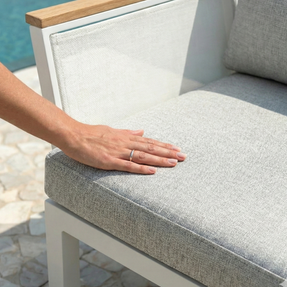 Hand pressing cushion of Sierra 5-Seater Outdoor Lounge Set in Grey, featuring a white metal frame, light-wood armrest, and pale gray upholstery, ideal for resort-style outdoor relaxation.