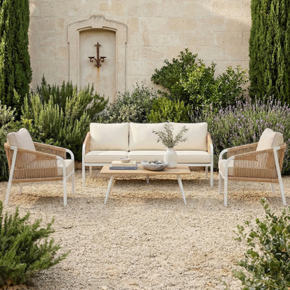 4-piece outdoor lounge set with white aluminum frames, tan woven rope sides, and cream cushions in a Mediterranean garden setting.