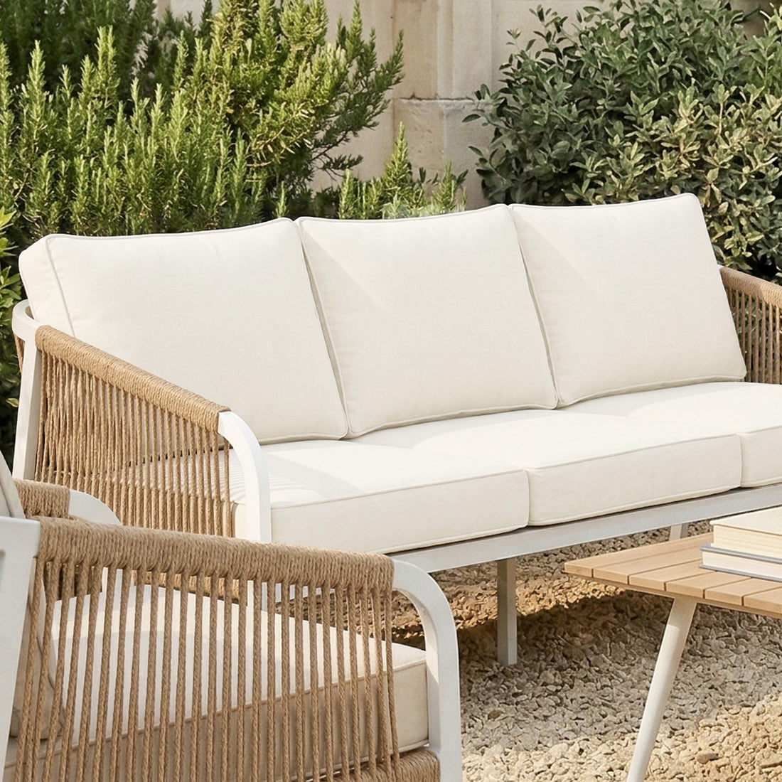 Close-up of a white aluminum outdoor sofa featuring vertical tan rope detailing on the armrests and plush cream-colored cushions.