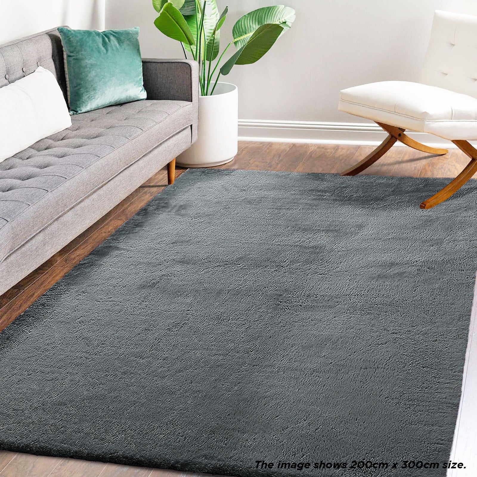 Azaliya Dark Grey Faux Rabbit Fur Rug 200x300cm displayed in a modern living room, complementing a gray sofa and white lounge chair, enhancing the space's cozy, contemporary aesthetic.