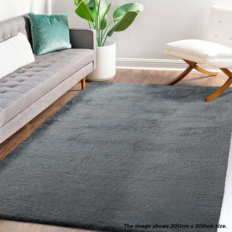 Azaliya Dark Grey Faux Rabbit Fur Rug 200x300cm displayed in a modern living room, complementing a gray sofa and white lounge chair, enhancing the space's cozy, contemporary aesthetic.