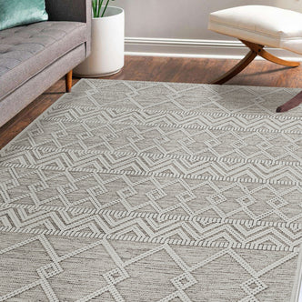 Benita Modern Abstract Tufted Rug 120x180cm with geometric patterns lies on hardwood, enhancing a cozy living room corner with a gray sofa, green cushion, houseplant, and cream ottoman.