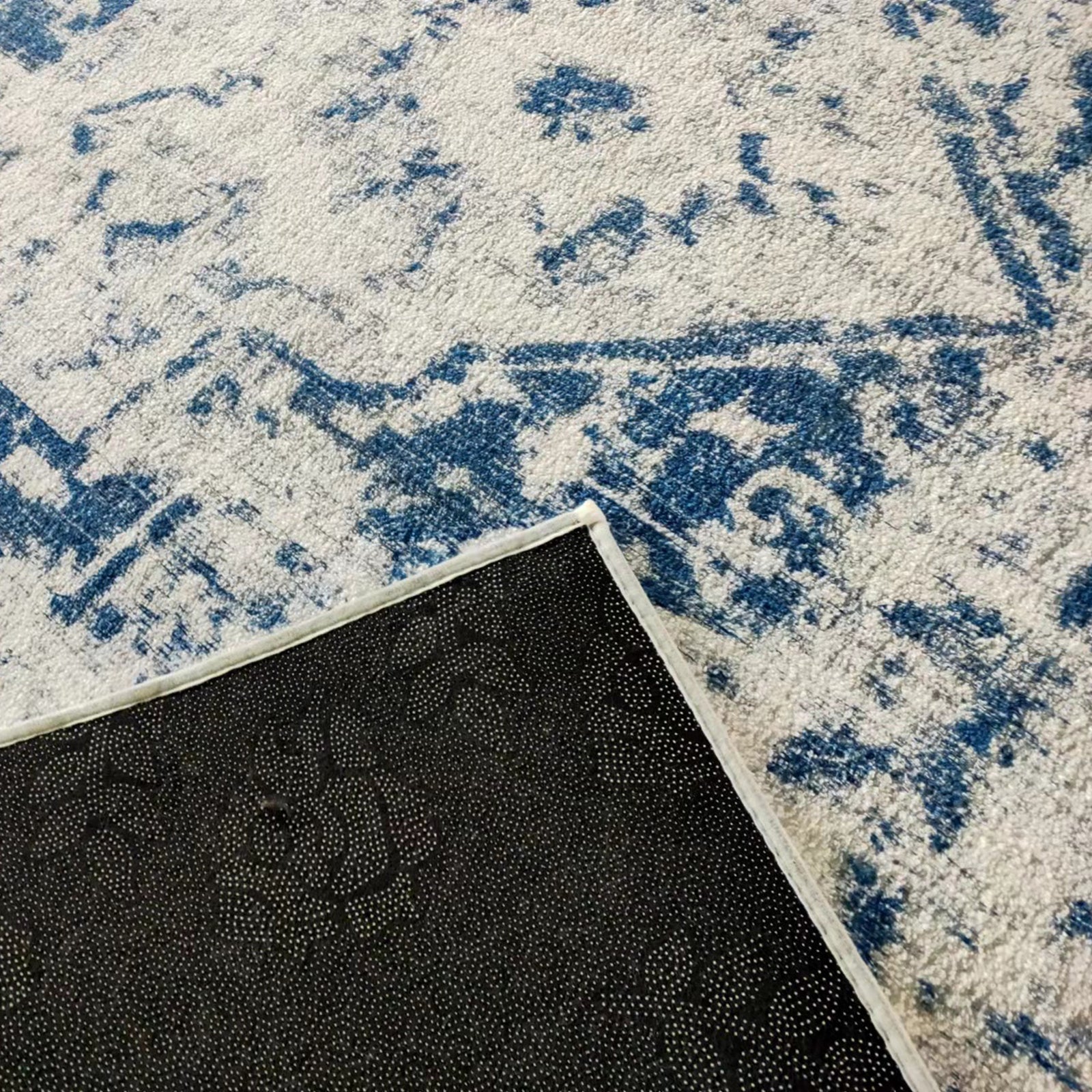 Boda 200x300cm Distressed Persian Silky Indoor Floor Rug with light cream pile, abstract blue pattern, and flipped corner showing black non-slip backing with grippy studs.
