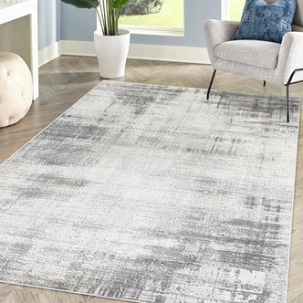 Franco 120x180cm Small Tufted Contemporary Indoor Rug featuring a subtle abstract gray-and-white pattern on a herringbone wood floor, complemented by a modern chair, ottoman, and potted plant.