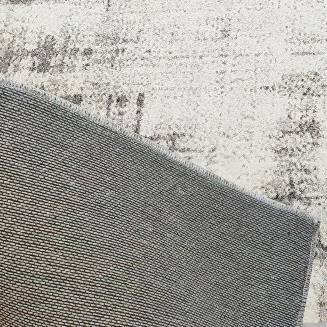 Franco Polyester Tufted Contemporary Floor Rug 160 x 230cm partially flipped, revealing its anti-slip backing on a speckled cream and grey floor, showcasing a tightly woven, rectangular-patterned design.