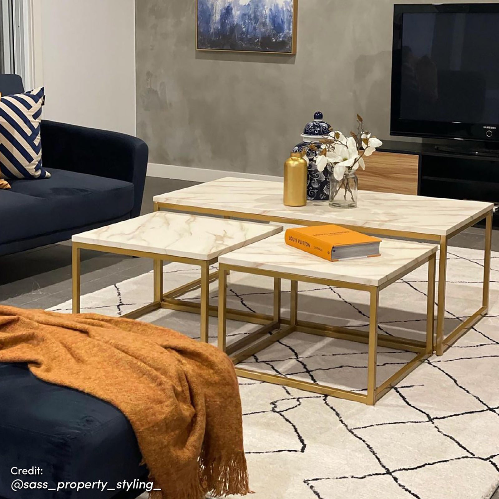 The Melody Black and White Modern Floor Rug 200 x 300cm features abstract black lines on an ivory backdrop, beneath a trio of nesting tables with a blue-and-white ginger jar and orange book.