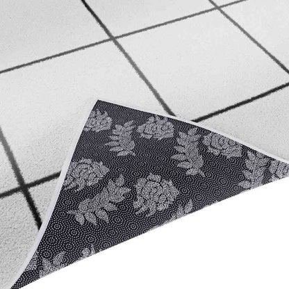 Milani 160x230cm Contemporary Printed Indoor Floor Rug features a light off-white pile with a black grid pattern. A flipped corner shows the backing's dark layer with a white, dotted rose-and-leaf motif.