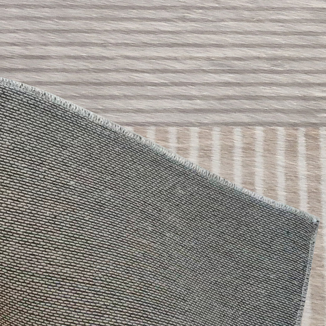 Corner view of Olivia 200x300cm Polyester Tufted Modern Abstract Indoor Rug, showcasing tightly-woven grey fabric with overlocked stitching on a light wood surface.