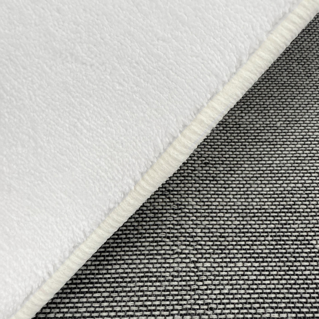 Close-up of Parna 200 x 300cm Curved Shaggy Rug in Cream White, showcasing soft, fleecy texture with overlocked border, layered over tightly woven gray fabric for contrast.