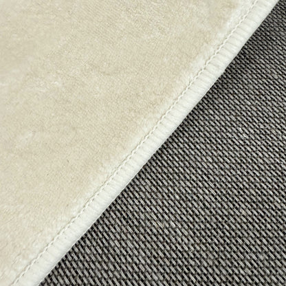 Close-up of Pavla 200 x 300cm Oval Shaggy Rug in Beige, showcasing the plush cream microfiber texture meeting a gray woven textile, highlighting its soft, shaggy design and stitched seam detailing.