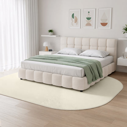 Pavla 200 x 300cm Oval Soft Rug in Beige under a plush, upholstered platform bed, featuring a thick, shaggy texture and an elegant, flowing shape, enhancing the room's minimalist, Scandinavian-inspired design.