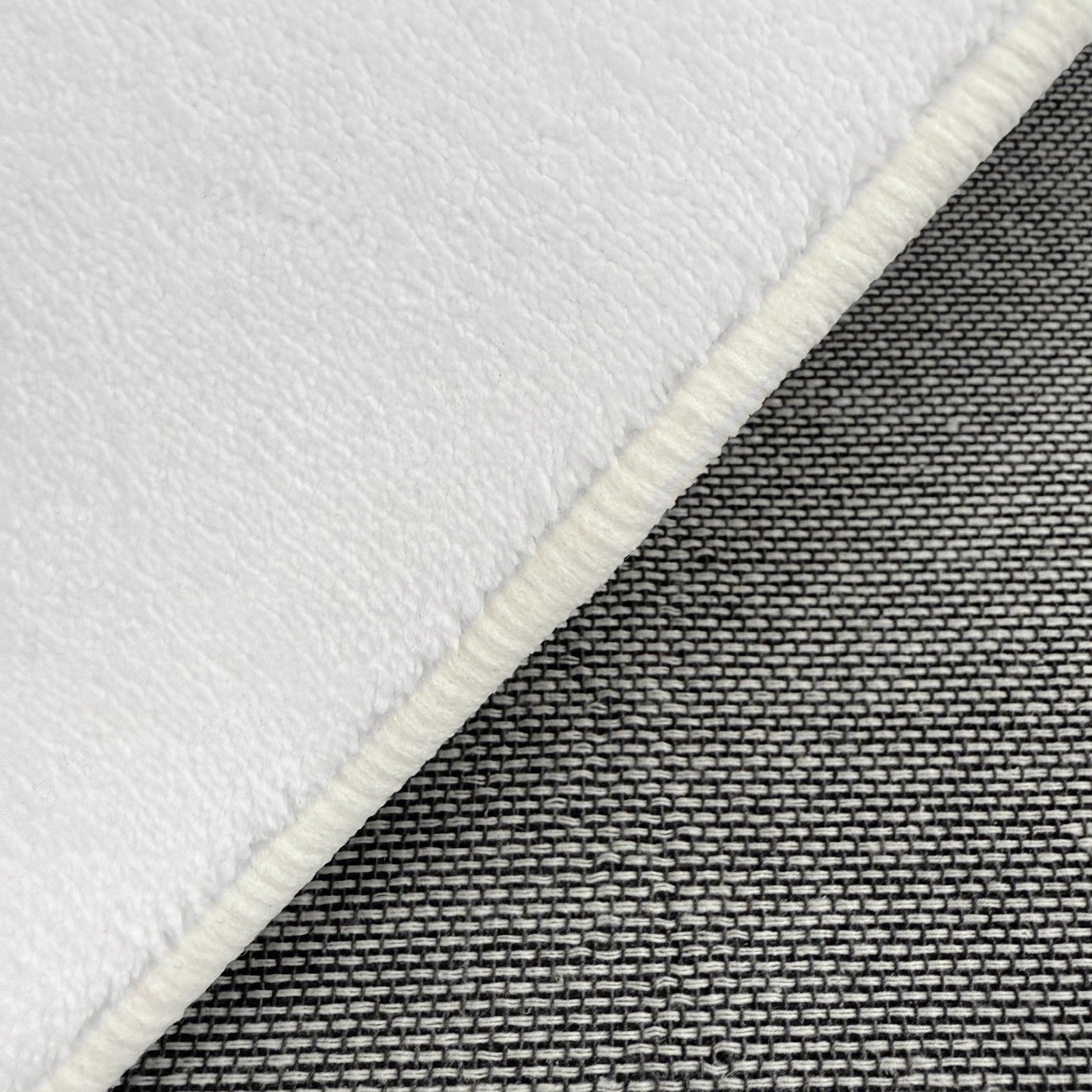 Close-up of Pixie 240x330cm Large Wavy Shag Rug in Cream White, showcasing its soft, fleece-like texture with a bound edge atop a woven grey-tone fabric background.