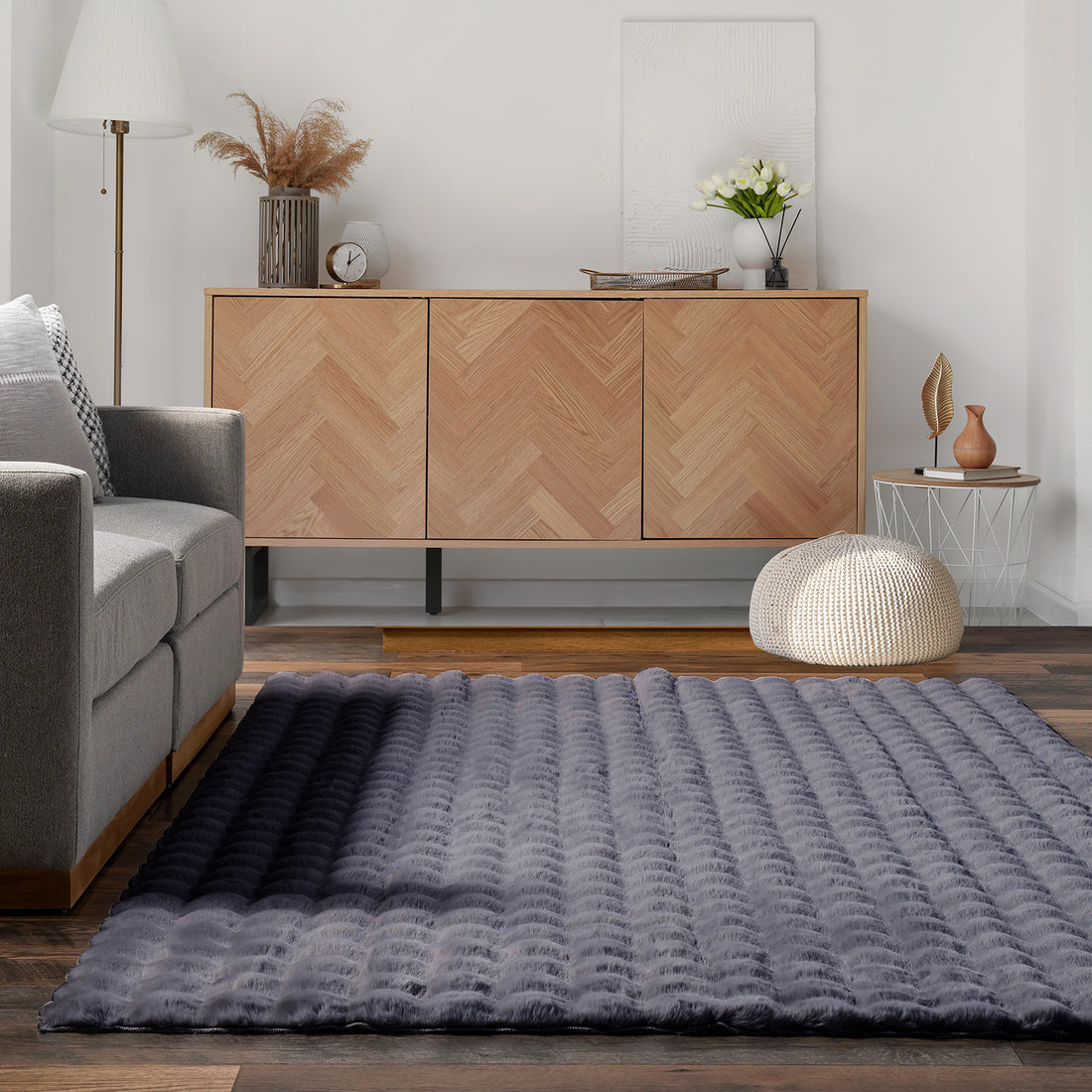 Severa 180x300cm Fluffy Fur Textured Bubble Rug Grey on dark wood floor, plush and quilted, complements light-grey sofa and herringbone-patterned sideboard, with cozy, modern living room accents.