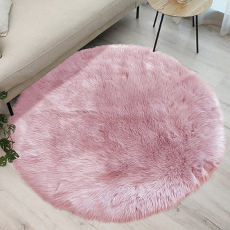 Cozy corner with a Shaddi 120cm Round Shaggy Soft Fluffy Fur Rug in Pink on light wood floor, bordered by beige sofa and wooden side table, complemented by green plant foliage.