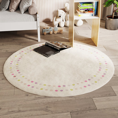 Shirin 160 Round Polka Dot Kids Indoor Rug on light wood flooring, cream with pastel dots, an open book centered. Nearby, white bed frame, wooden toy train, white teddy bears, and children's books.