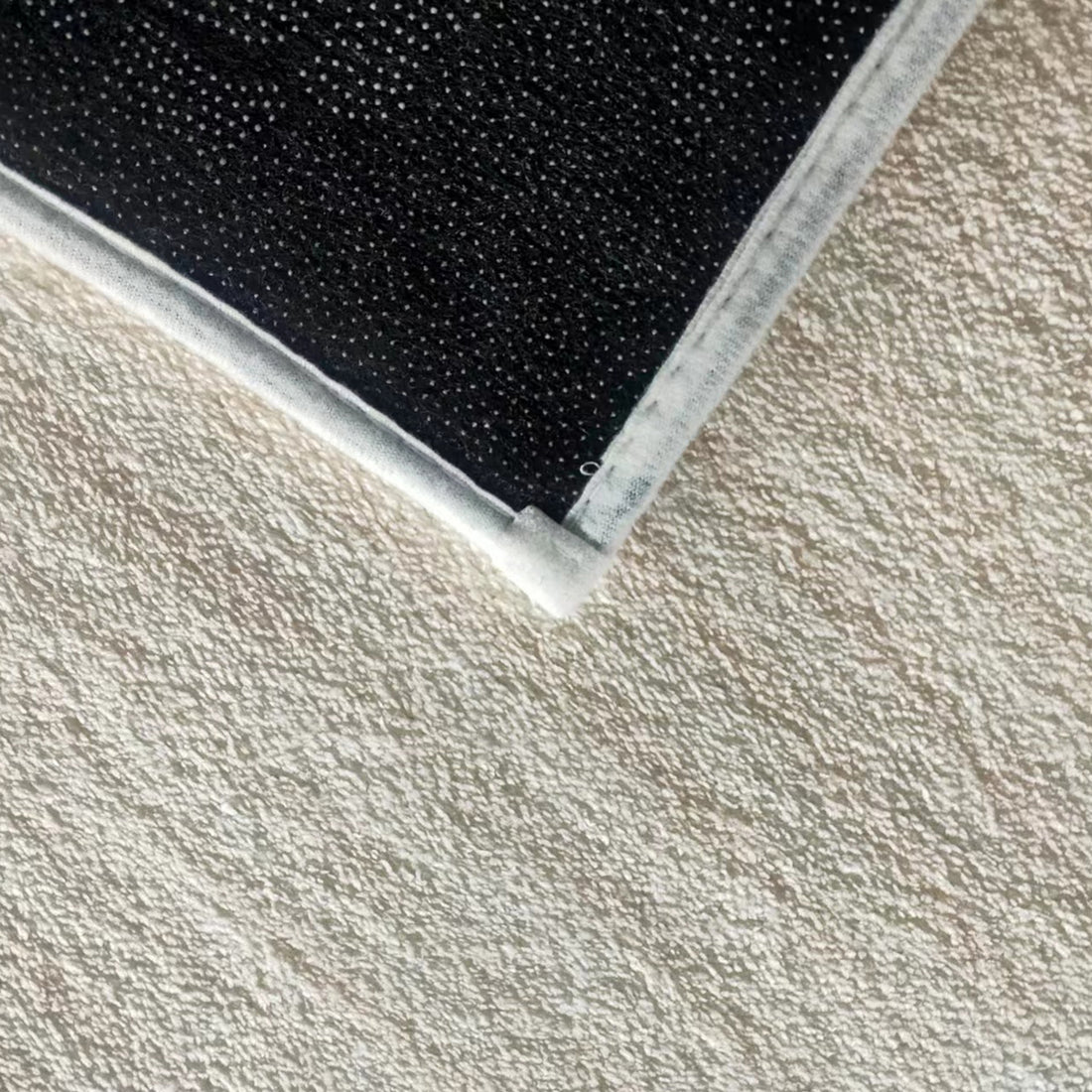 Close-up of Vastra 200x300cm Modern Abstract Floor Rug, showcasing its black fabric pad corner with white stitched edges on a textured surface, highlighting its subtle woven pattern.