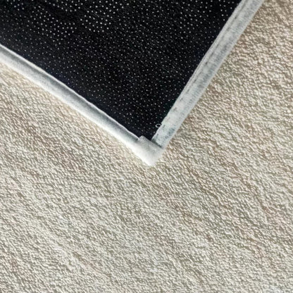 Close-up of Vastra 200x300cm Modern Abstract Floor Rug, showcasing its black fabric pad corner with white stitched edges on a textured surface, highlighting its subtle woven pattern.