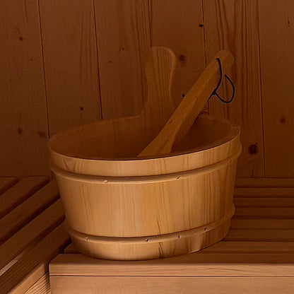 Medika 8 Person Traditional Finnish Outdoor Sauna featuring a wooden bucket and ladle on a wooden bench inside, highlighting the spacious, authentic Finnish design ideal for backyard relaxation.