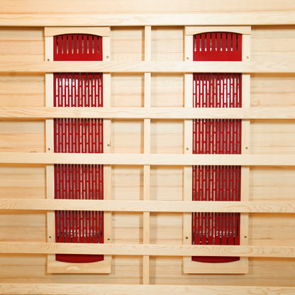 Taavi 2 Person Ceramic Infrared Indoor Home Sauna with vertical red infrared-heating panels on light wood backing, enclosed by a horizontal slat framework, and resting on a matching wood floor.