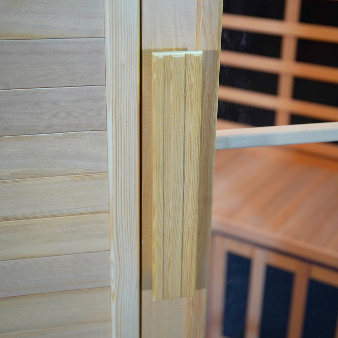 Taavi 4 Person Corner Carbon Fibre Infrared Indoor Sauna features a light-toned wooden door with a vertical wood handle on a glass panel, revealing a warm sauna interior with slatted benches.