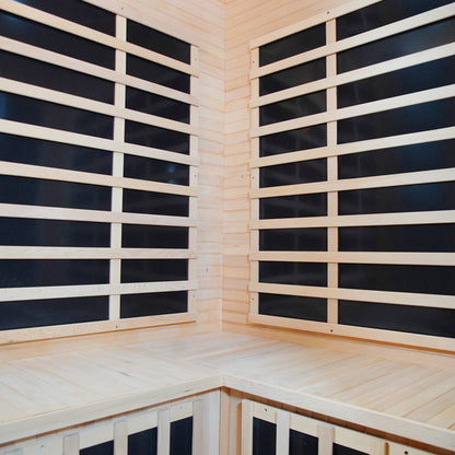 Taavi 4-Person Corner Carbon Fibre Infrared Indoor Sauna with light-colored wooden panels, benches, and black heater panels behind horizontal slats, offering a private, infrared-heated sanctuary designed for relaxation and wellness.