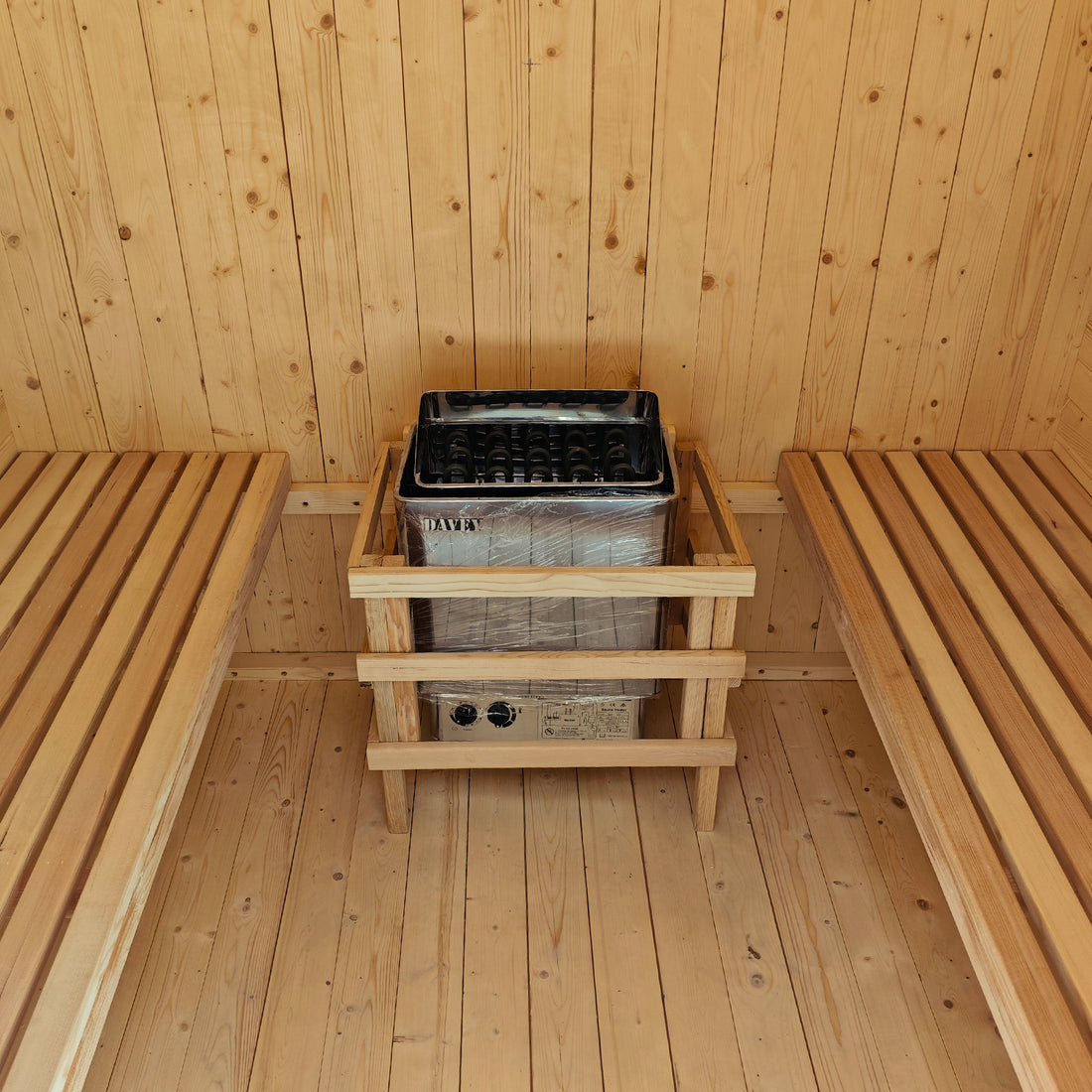 The Tarni 2-Person Finnish Outdoor Sauna – Fir Wood features twin slatted benches and an electric heater with a protective guard, set in a light-colored wood-paneled interior.