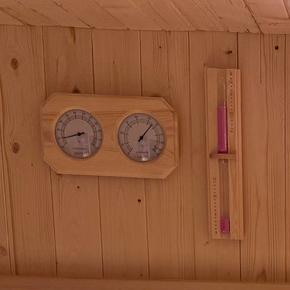 Tarni 2-Person Finnish Outdoor Sauna interior wall with a mounted thermometer and hygrometer, alongside a wooden-framed sand-glass timer with pink sand, enhancing your relaxation experience.