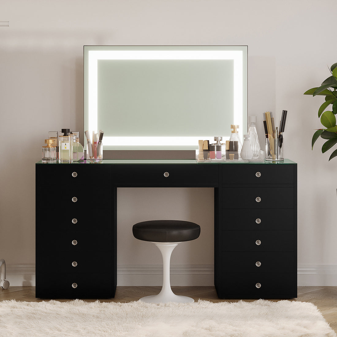 Adeline LED Mirror Storage Dressing Table in Black with glass top, LED-lit mirror, and 13 drawers. Features assorted cosmetics on top, a white stool, and a plush rug beneath.