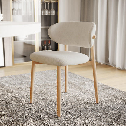 Audrey Curved Fabric Dining Chair Set of 2 in Beige features light-wood frames, off-white upholstered seats, and backrests, placed on a gray rug in a modern dining area with a round table and cabinet.