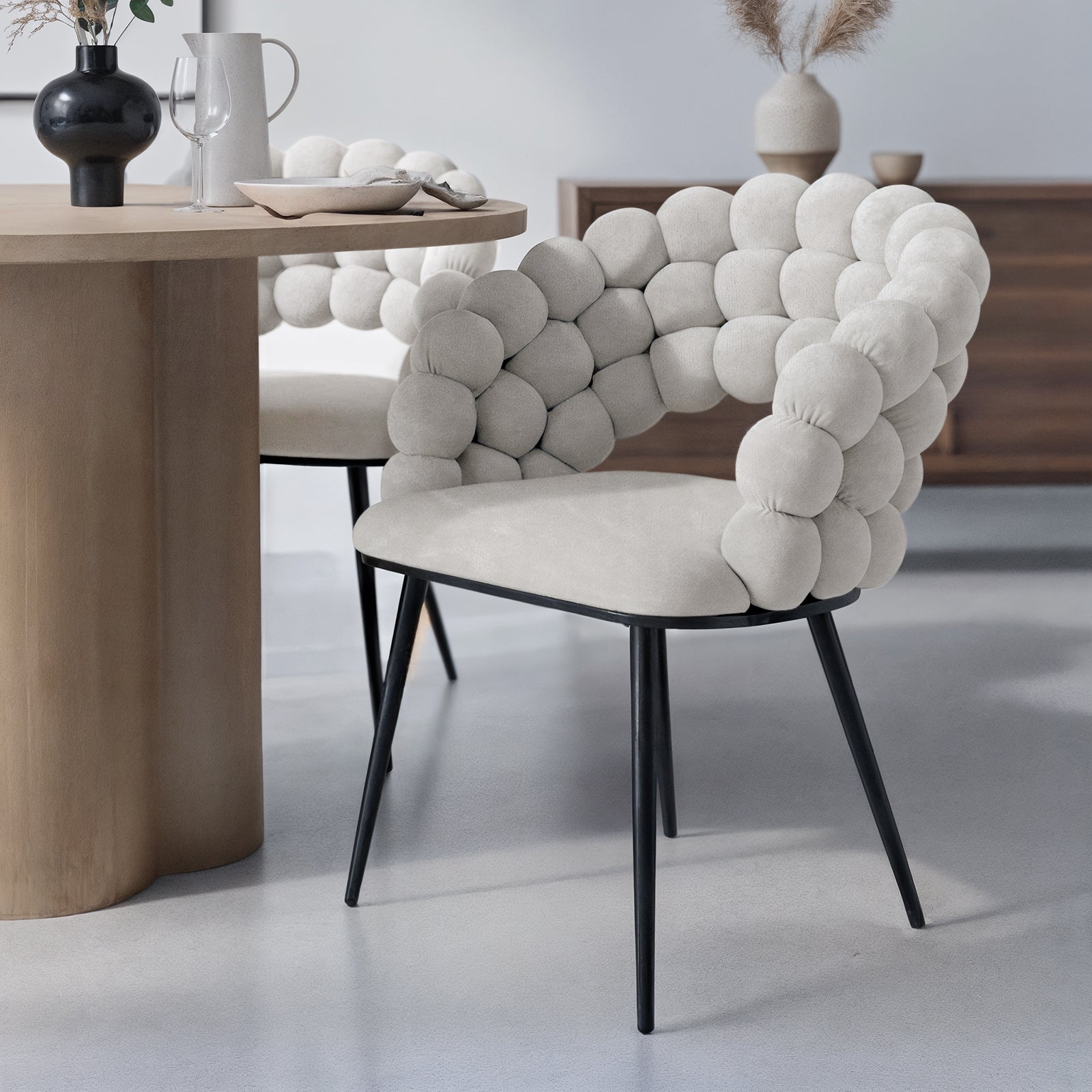 Claudine Velvet Curved Dining Chair Set of 2 in Warm Grey, featuring bubble-style upholstered back, black metal legs, and a minimalist design, paired with a light wood table in a modern dining setup.