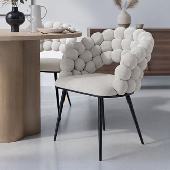 Claudine Velvet Curved Dining Chair Set of 2 in Warm Grey, featuring bubble-style upholstered back, black metal legs, and a minimalist design, paired with a light wood table in a modern dining setup.